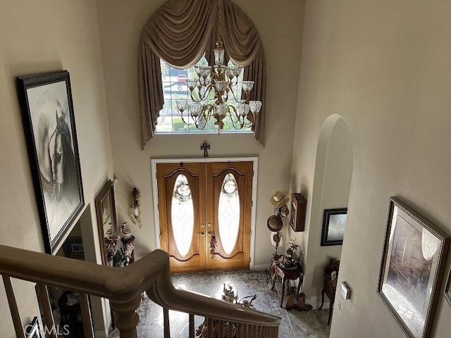 foyer entrance with arched walkways, french doors, a high ceiling, and an inviting chandelier