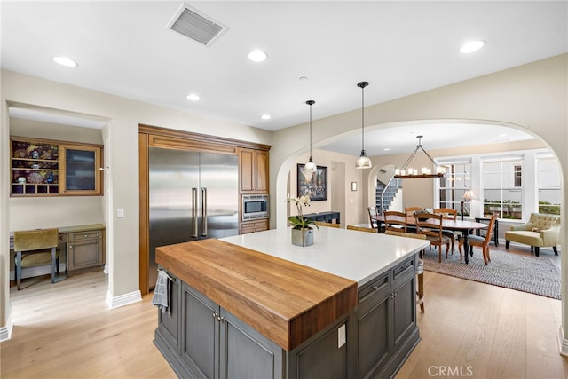 kitchen featuring light wood finished floors, visible vents, arched walkways, and built in appliances