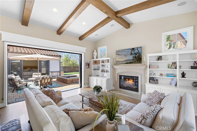 living room featuring light wood-type flooring, a glass covered fireplace, lofted ceiling with beams, and recessed lighting