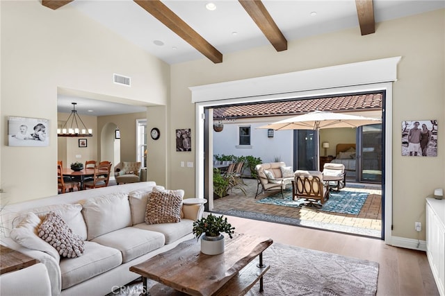 living area featuring visible vents, a towering ceiling, an inviting chandelier, wood finished floors, and beamed ceiling