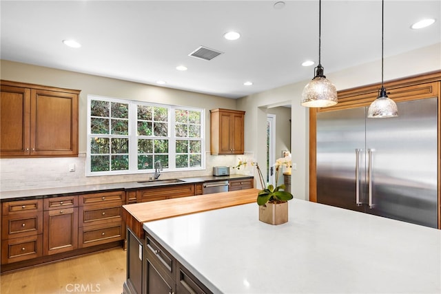 kitchen featuring light wood finished floors, stainless steel appliances, tasteful backsplash, visible vents, and a sink