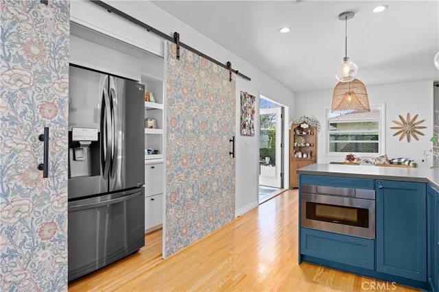 kitchen with light wood finished floors, hanging light fixtures, a barn door, appliances with stainless steel finishes, and blue cabinets