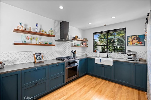 kitchen with blue cabinets, stainless steel appliances, open shelves, a sink, and wall chimney exhaust hood