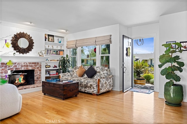 living area with built in shelves, a brick fireplace, wood finished floors, and a healthy amount of sunlight