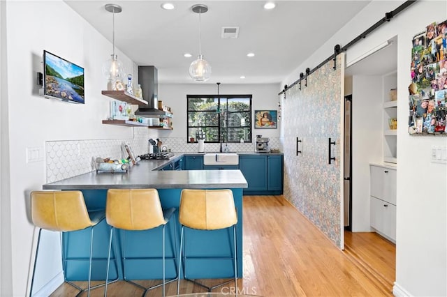 kitchen with open shelves, a barn door, a sink, ventilation hood, and blue cabinets