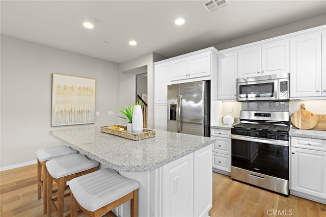 kitchen with appliances with stainless steel finishes, light wood-style floors, visible vents, and a center island