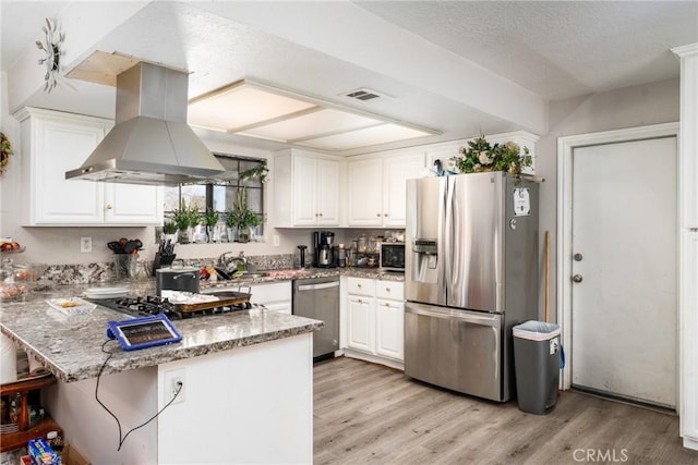 kitchen with white cabinets, a peninsula, light stone countertops, island exhaust hood, and stainless steel appliances