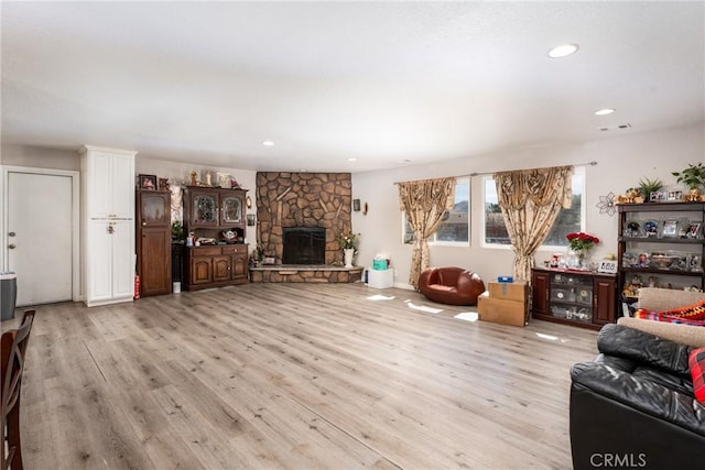 living room with light wood-type flooring, visible vents, a stone fireplace, and recessed lighting