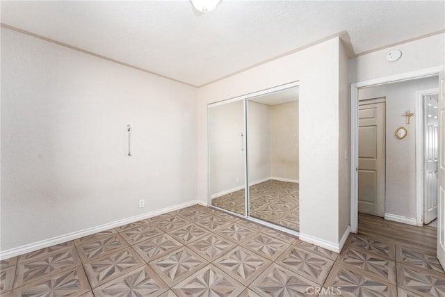 unfurnished bedroom with light floors, a closet, crown molding, and baseboards