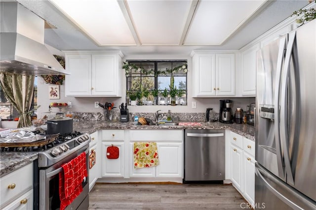 kitchen featuring stainless steel appliances, a sink, white cabinetry, light wood-type flooring, and wall chimney exhaust hood