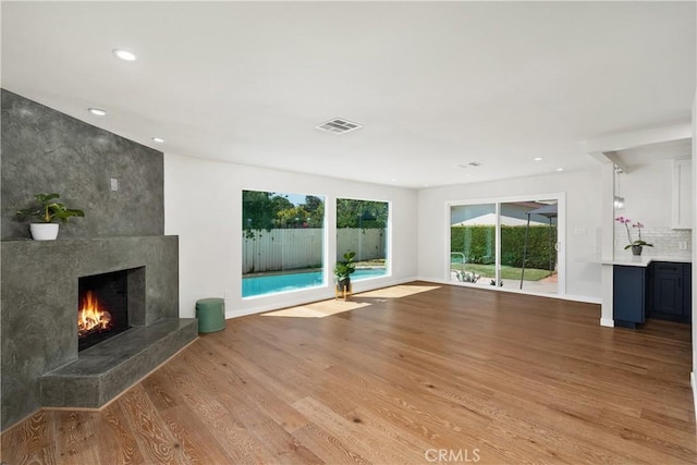 unfurnished living room featuring recessed lighting, visible vents, a tiled fireplace, wood finished floors, and baseboards