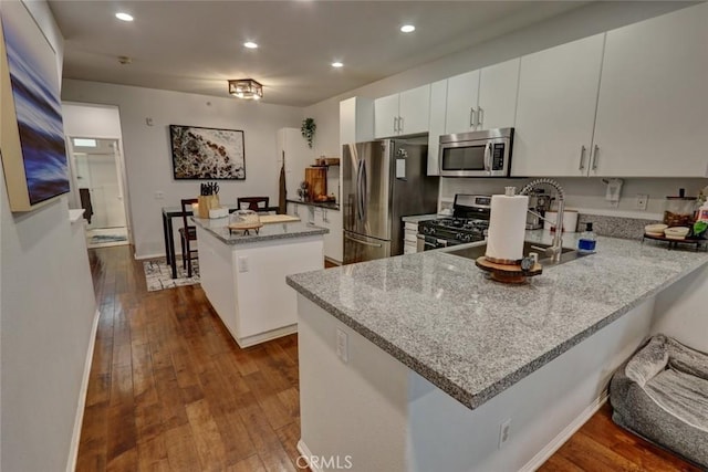 kitchen featuring dark wood finished floors, a kitchen island, appliances with stainless steel finishes, a peninsula, and light stone countertops