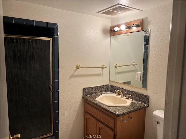 bathroom with vanity, visible vents, a stall shower, toilet, and a textured wall