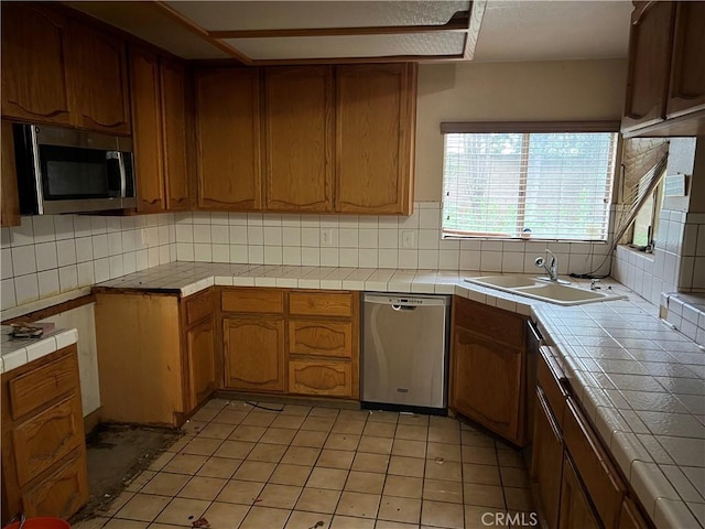 kitchen with tile counters, stainless steel appliances, tasteful backsplash, and a sink