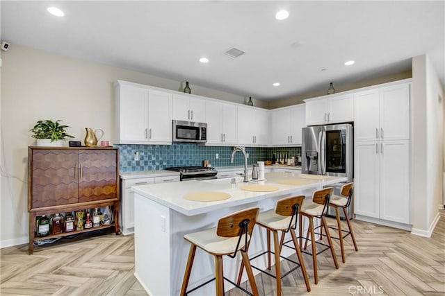 kitchen with white cabinets, decorative backsplash, appliances with stainless steel finishes, light countertops, and a kitchen bar