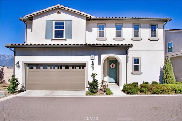 mediterranean / spanish-style home with a garage, decorative driveway, a tile roof, and stucco siding