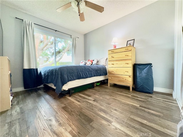 bedroom with a ceiling fan, a textured ceiling, baseboards, and wood finished floors