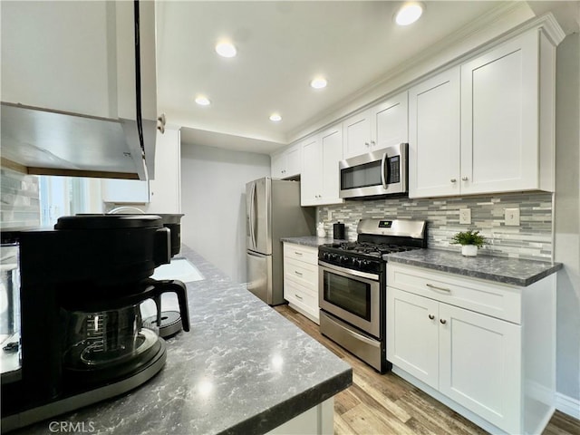 kitchen with light wood finished floors, white cabinetry, appliances with stainless steel finishes, and backsplash