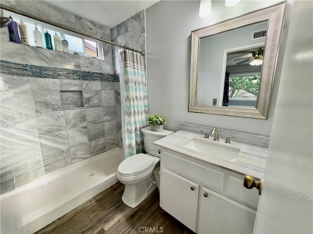 bathroom featuring visible vents, toilet, vanity, wood finished floors, and tiled shower