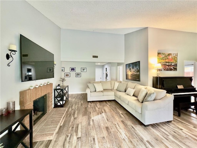 living area featuring a brick fireplace, visible vents, a textured ceiling, and wood finished floors