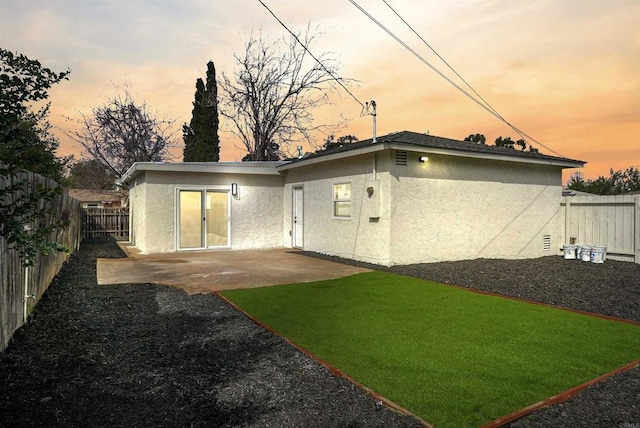 back of property at dusk with a yard, a patio area, a fenced backyard, and stucco siding