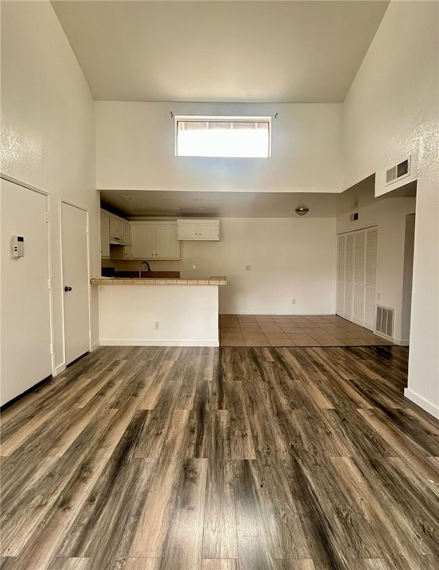 unfurnished living room featuring a towering ceiling, visible vents, and dark wood-style flooring