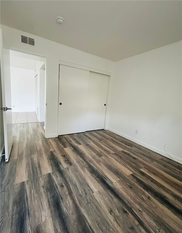 unfurnished bedroom featuring dark wood-style floors, baseboards, visible vents, and a closet