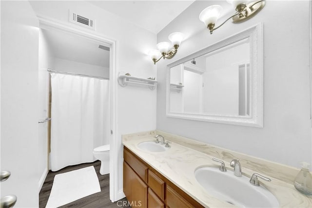 bathroom featuring toilet, double vanity, visible vents, and a sink