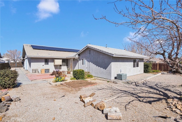 rear view of property with stucco siding, fence, cooling unit, and roof mounted solar panels