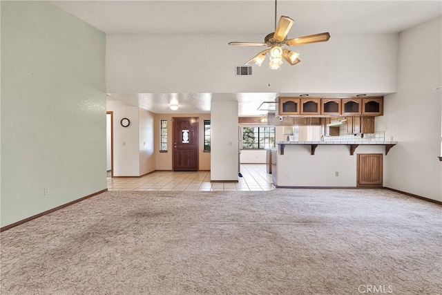 unfurnished living room featuring light carpet, light tile patterned floors, ceiling fan, and a high ceiling