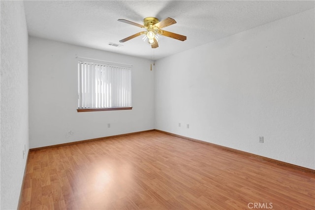 spare room with ceiling fan, a textured ceiling, baseboards, and wood finished floors