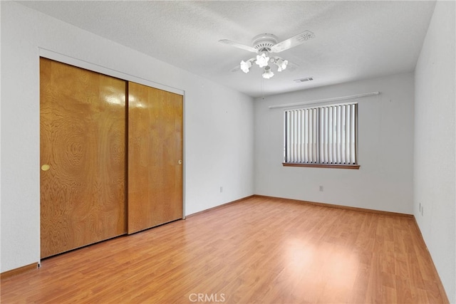 unfurnished bedroom featuring a textured ceiling, a closet, wood finished floors, and visible vents