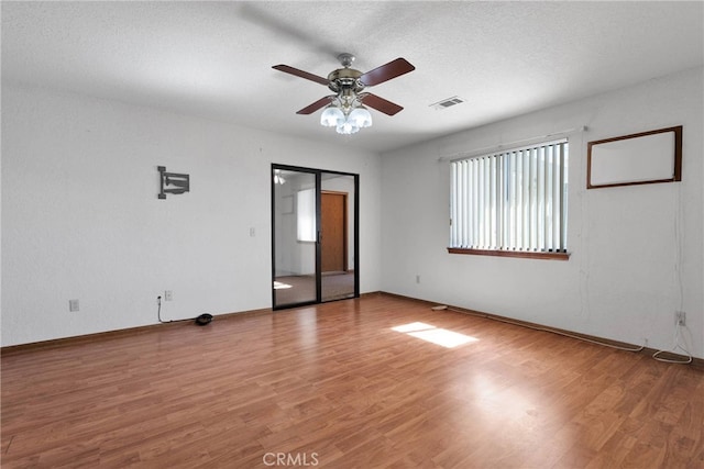 spare room featuring a textured ceiling, ceiling fan, wood finished floors, visible vents, and baseboards