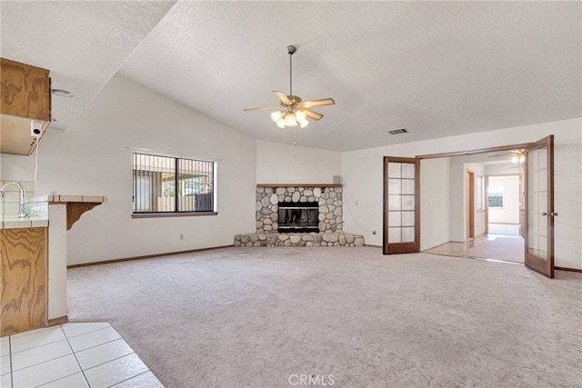 unfurnished living room featuring a textured ceiling, light carpet, a fireplace, a ceiling fan, and french doors