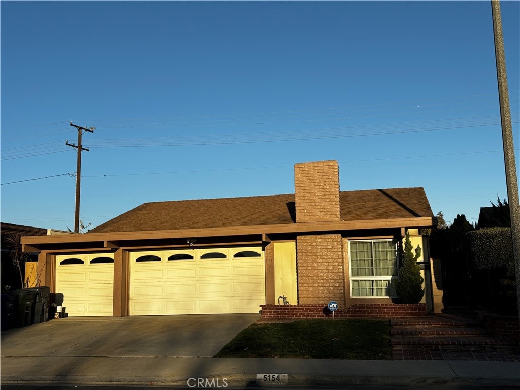 ranch-style house with an attached garage, a chimney, concrete driveway, and brick siding