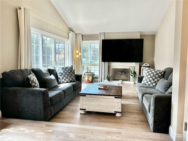 living room with a glass covered fireplace, wood finished floors, and vaulted ceiling