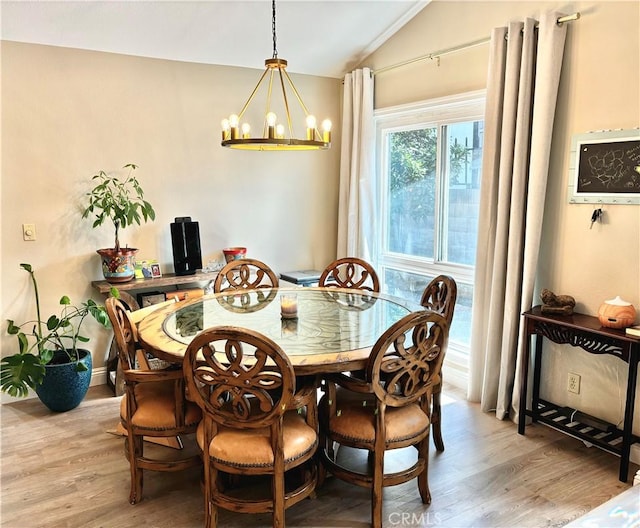 dining area with light wood-type flooring, a notable chandelier, and vaulted ceiling