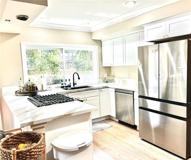 kitchen featuring light stone countertops, ornamental molding, appliances with stainless steel finishes, a peninsula, and a sink
