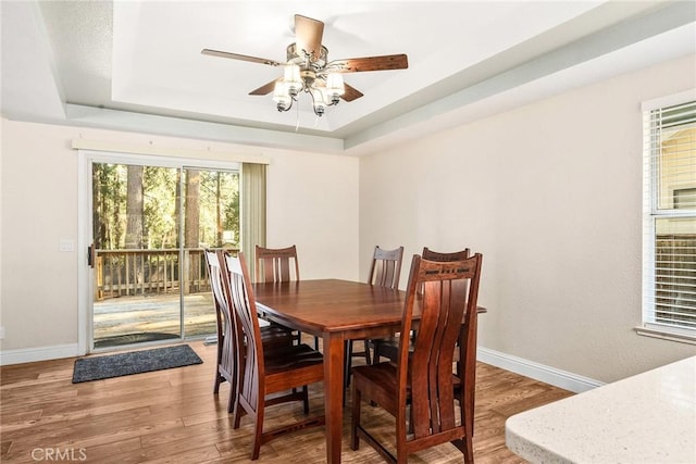 dining area with a tray ceiling, light wood-style flooring, and baseboards