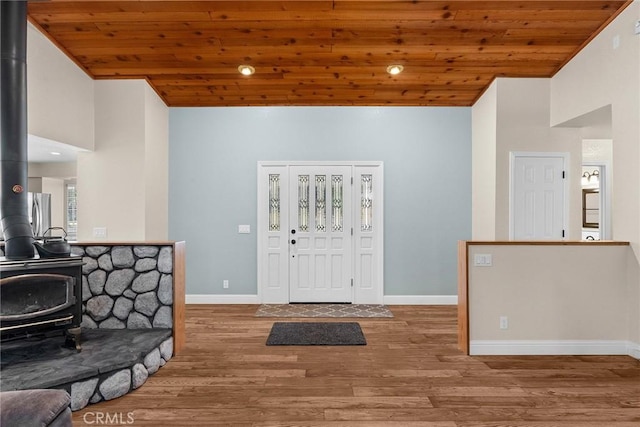 foyer entrance with a wood stove, wood finished floors, high vaulted ceiling, wooden ceiling, and baseboards