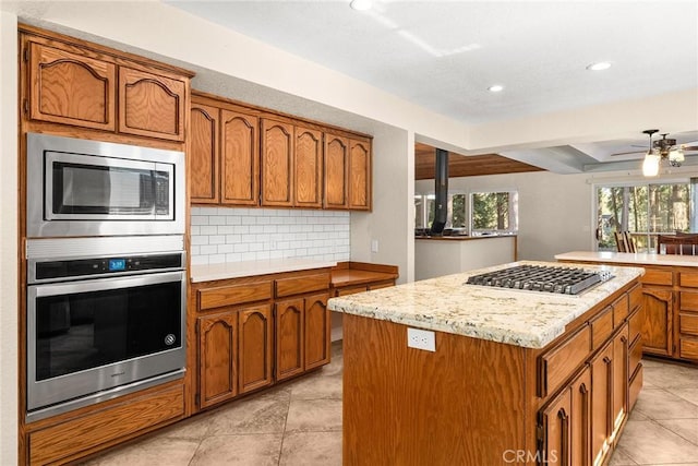 kitchen with tasteful backsplash, ceiling fan, a kitchen island, appliances with stainless steel finishes, and brown cabinets