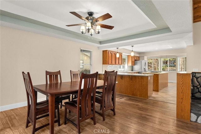 dining area with a tray ceiling, baseboards, ceiling fan, and light wood finished floors