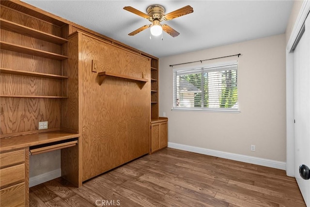 interior space with built in desk, a closet, wood finished floors, and baseboards