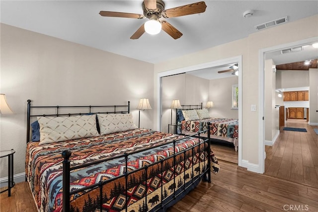 bedroom with a closet, visible vents, hardwood / wood-style floors, a ceiling fan, and baseboards