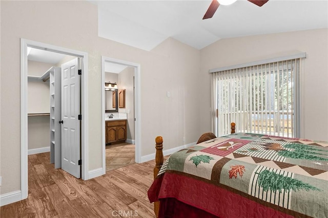 bedroom with light wood-style flooring, a spacious closet, vaulted ceiling, ensuite bath, and baseboards