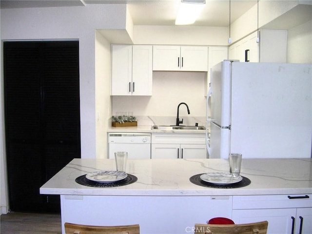 kitchen with white appliances, a sink, white cabinetry, and light stone countertops