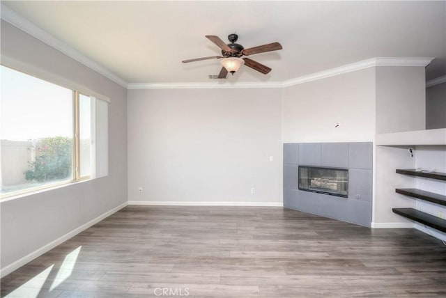 unfurnished living room featuring ornamental molding, baseboards, a tiled fireplace, and wood finished floors