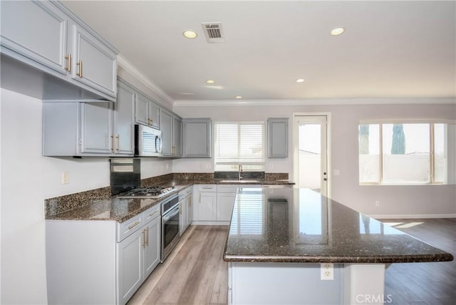 kitchen featuring light wood-type flooring, dark stone counters, stainless steel appliances, and crown molding