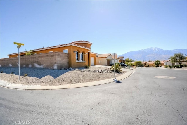 exterior space featuring a tile roof, concrete driveway, an attached garage, a mountain view, and fence