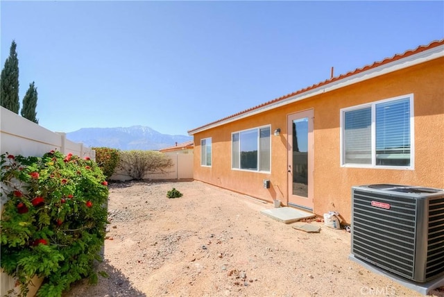 rear view of property with a fenced backyard, a mountain view, central AC, and stucco siding